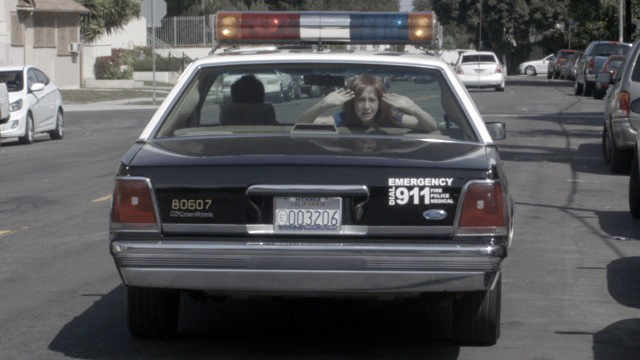 Young Raven (Jessica Bassuk) is being taken away in a police car