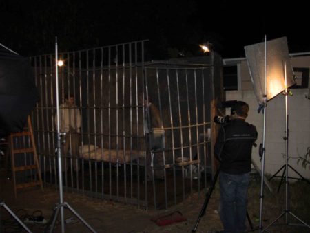Jail set lit for filming, actors in set, Bruce Heinsius behind camera